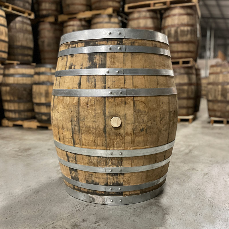 
                  
                    Side with bung of an Old Elk Armagnac Cask Finished Bourbon Barrel with other used barrels stacked on pallets in the background
                  
                