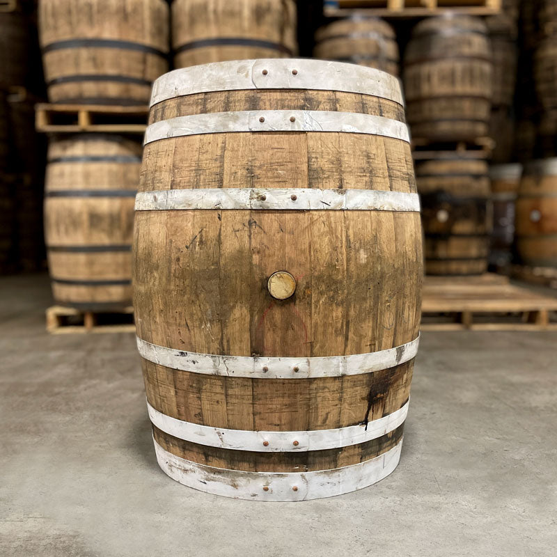 Side of an Old Elk Wheated Bourbon Light Char Barrel with other used bourbon barrels stacked on pallets in the background
