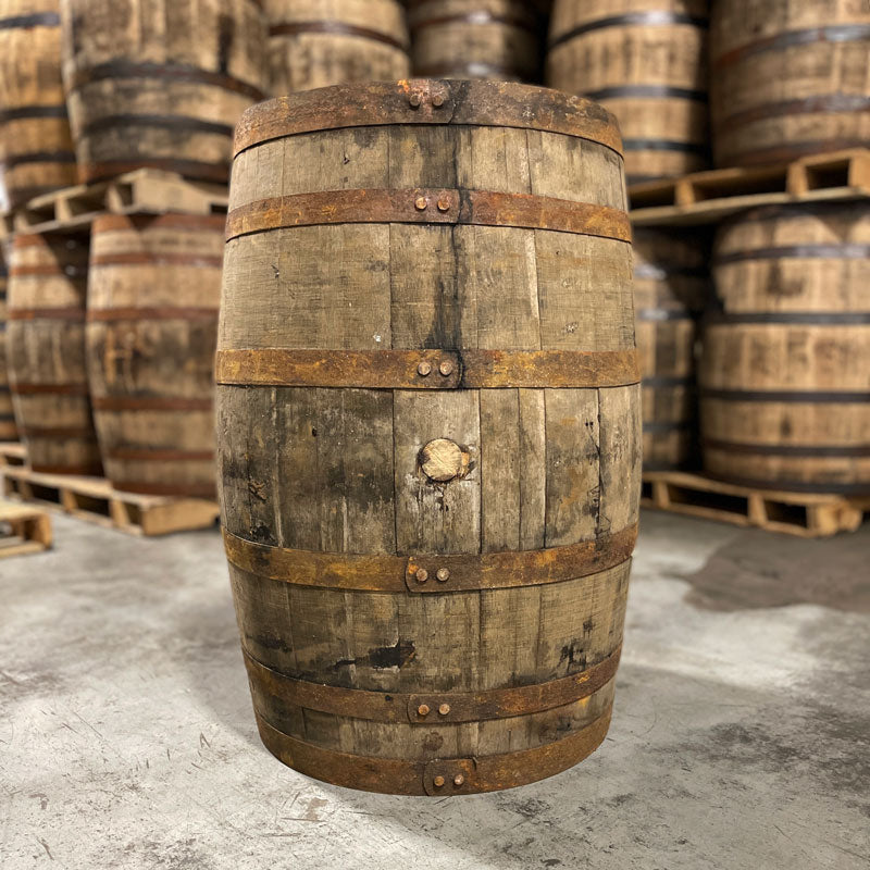 Side with bung of a 15 Year Widow Jane Bourbon Barrel with other used bourbon barrels stacked on pallets in the background