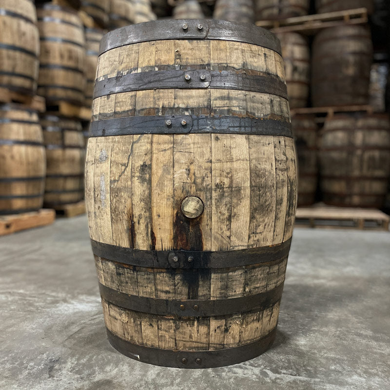 Side with bung of a Woodford Reserve Rye Whiskey Barrel with other used whiskey barrels stacked on pallets in the background