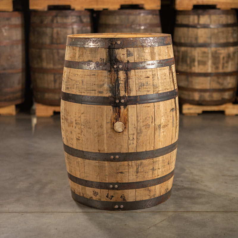 Side of a used 4 year Wild Turkey Bourbon barrel with other barrels stacked on pallets in the background