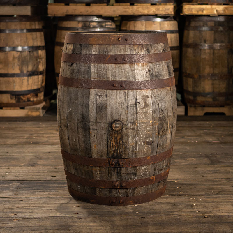 Barbados rum barrel ex-bourbon with rusted rings and dark, dirtied staves and barrels stacked on pallets in the background