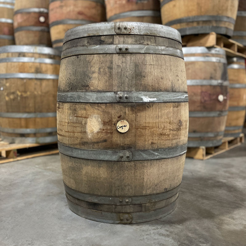 Side of a Cognac Cask 225L showing Cognac written on the bung and other used cognac and port casks stacked on pallets in the background