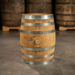 Side of a 10 Gallon Distillery 291 Rye Whiskey barrel with some handwriting on the barrel with distiller notes and other used whiskey barrels on pallets in the background