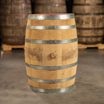 Side of a 30 Gallon FEW Spirits Bourbon barrel with shiny, steel bands and other used bourbon barrels on pallets in the background