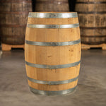 Side of a 30 Gallon Old Line Spirits Single Malt Whiskey Barrel with shiny, steel rings and other used whiskey barrels on pallets in the background