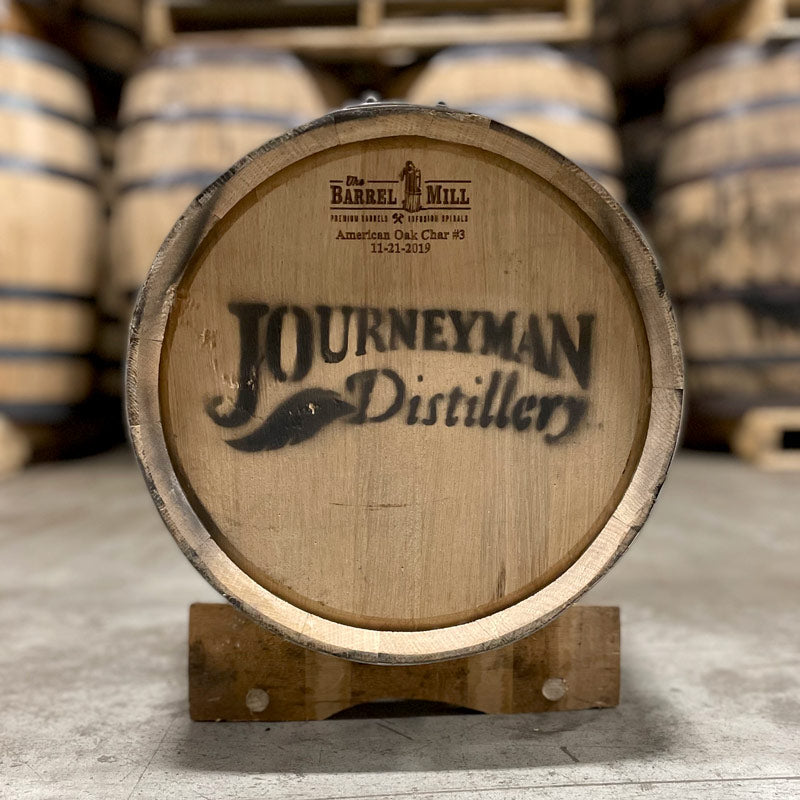 Other end of a 5 Gallon Journeyman Rum Barrel with distillery logo stamped on the head and barrel on a stand.