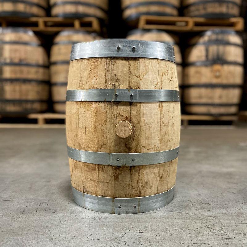 Side of a 5 gallon Brother Justus Single Malt Whiskey Barrel in front of used bourbon barrels stacked on pallets