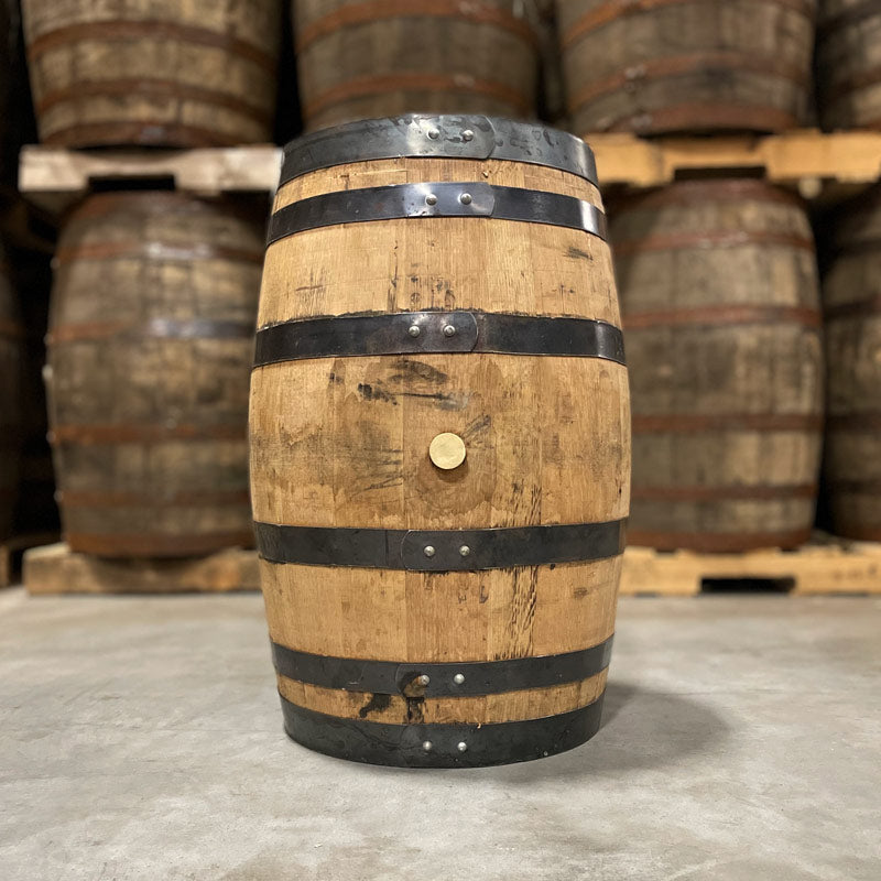 Side with bung of a 25 Gallon Rock Town Distillery Gin Barrel with other used barrels stacked on pallets in the background