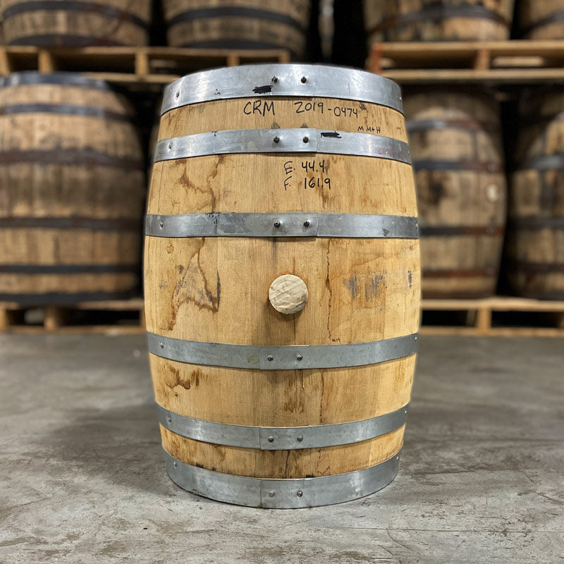 Side with bung of a 15 Gallon Distillery 291 Rye Whiskey Barrel with other used whiskey barrels stacked on pallets in the background