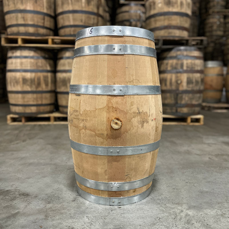 Side of a 20 Gallon Rock Town Bourbon Barrel with bunghole side visible and used bourbon barrels stacked on pallets in the background