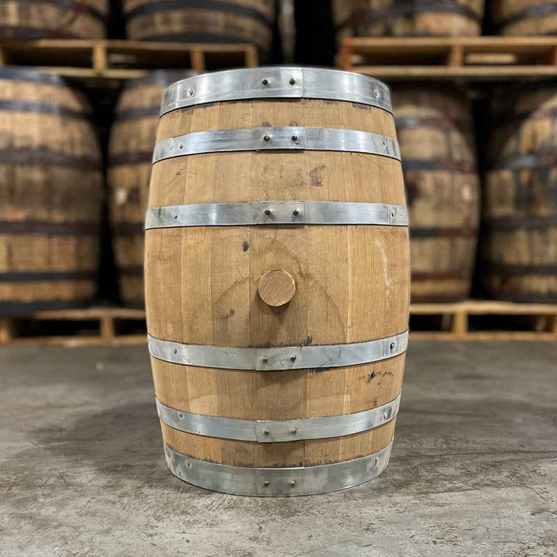 Side with bung of a 15 Gallon Lonely Oak Rye Whiskey Barrel with used whiskey barrels stacked on pallets in the background