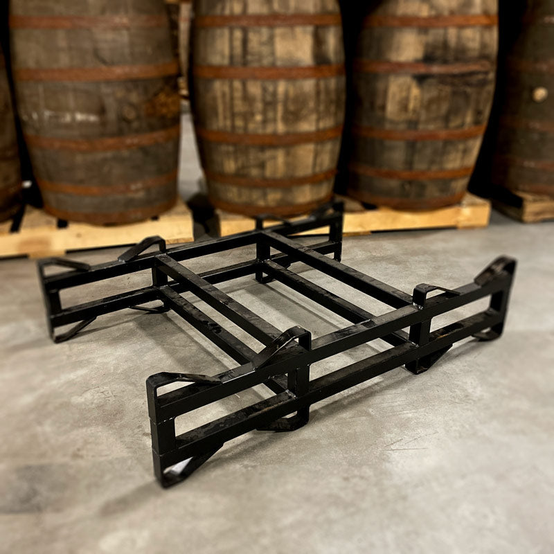 Used, black 2-barrel steel rack with 3-inch clearance height on floor in front of barrels stacked on pallets