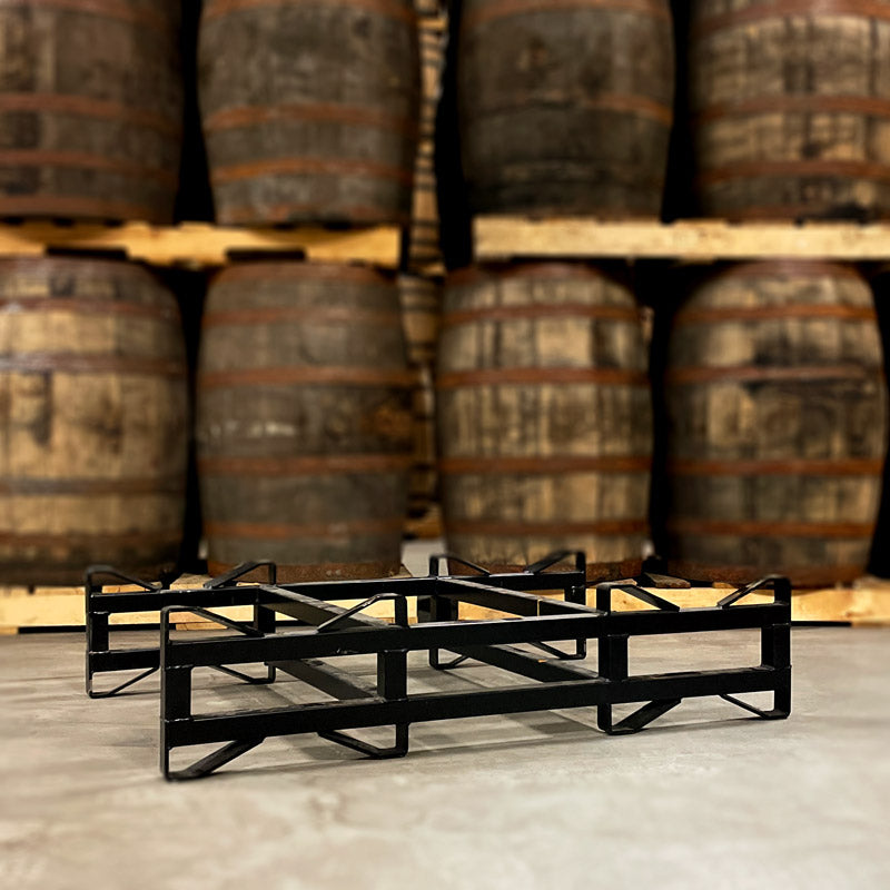 Used, black 2-barrel steel rack with 3-inch clearance height on floor in front of barrels stacked on pallets