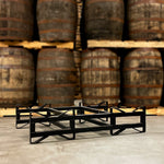 Used, black 2-barrel steel rack with 3-inch clearance height on floor in front of barrels stacked on pallets