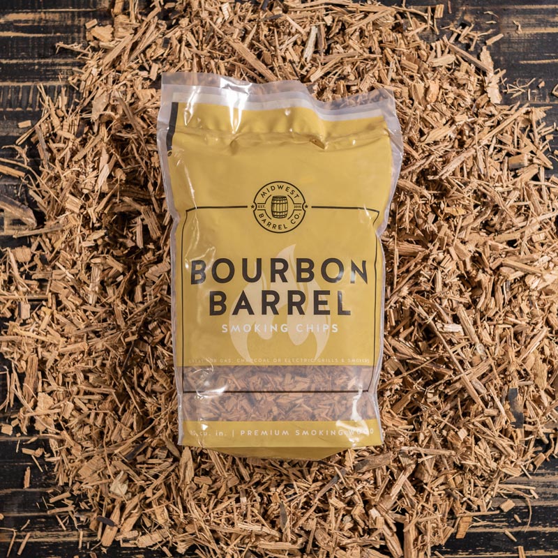 A bag full of Bourbon Barrel BBQ Smoking Wood Chips with used bourbon barrels in the background with loose chips around it