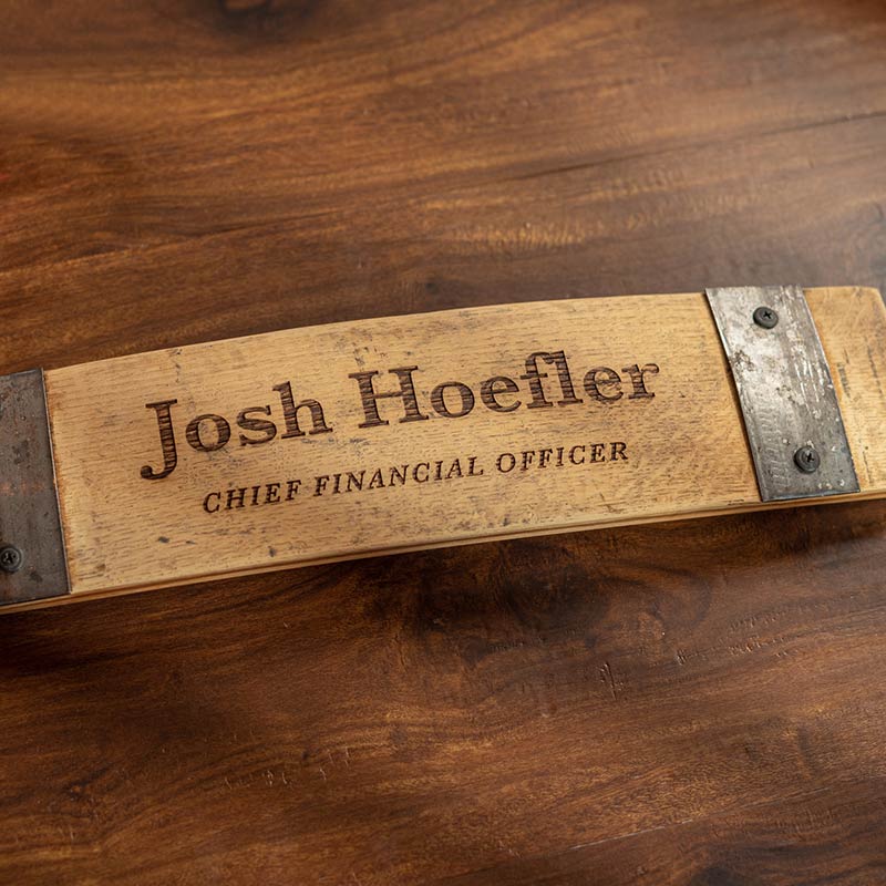 Whiskey barrel stave desk plate with a name and position engraved on the stave and two bands screwed into the wood on both sides