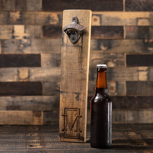 
                  
                    unopened beer bottle next to whiskey barrel stave bottle opener engraved with letter M in front of vertical rectangle
                  
                