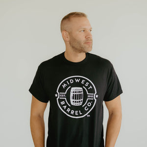 
                  
                    Man wearing black shirt with white Midwest Barrel Co. circle logo with Est. 2015 around a bourbon barrel in the middle of the circle
                  
                
