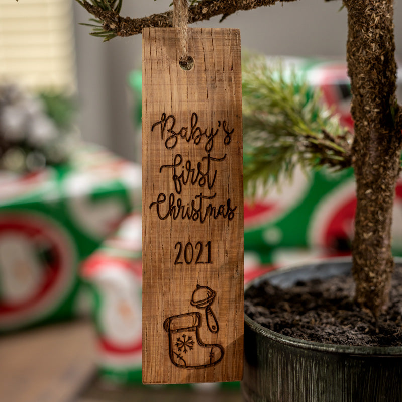 Baby's Frist Christmas Wine Barrel Stave ornament on a Christmas tree with a baby rattle and a snowflake on a stocking engraved on the ornament.