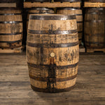 Jack Daniels whiskey barrel with dark, rustic rings and stained, dirtied wood and barrels stacked on pallets in the background